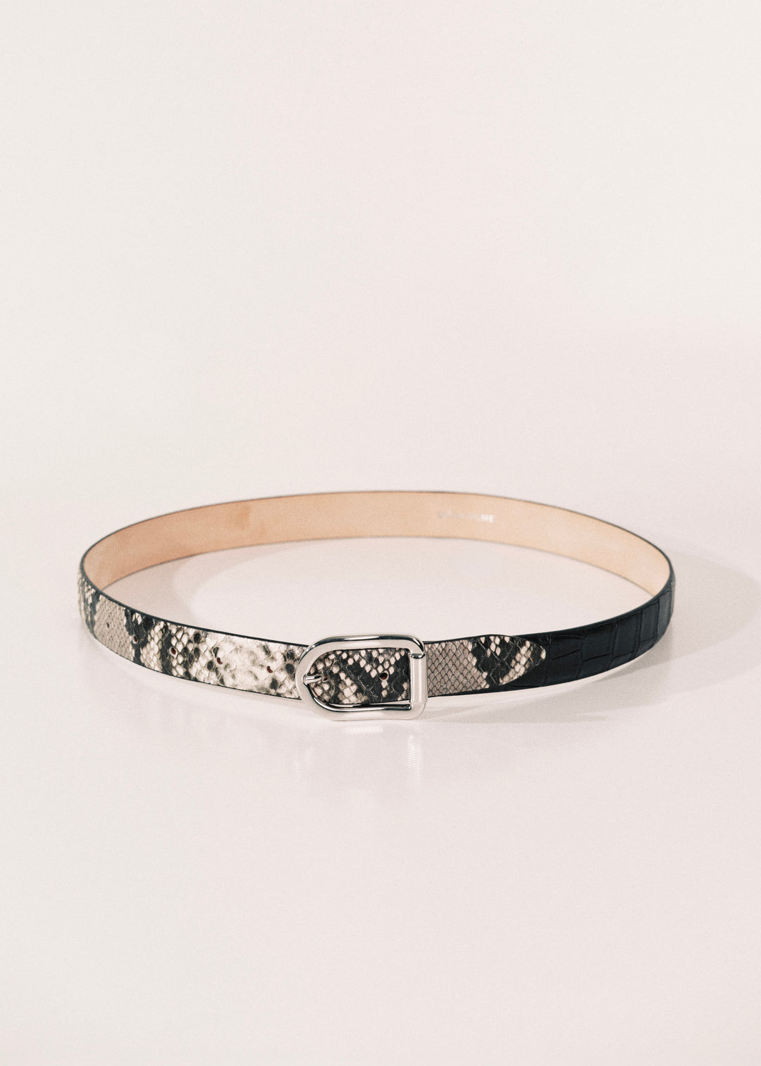 A slim belt with a black and white snakeskin pattern, featuring a silver-tone metal buckle and a beige inner lining, displayed on a clean white background.