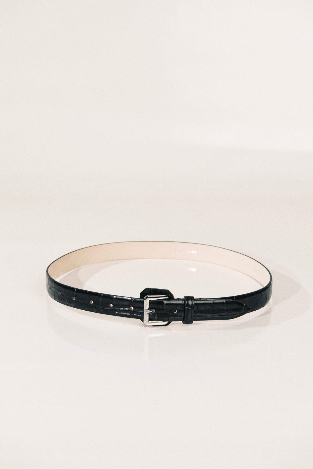 A black leather belt with a silver buckle, displayed in a circular shape on a clean white studio background.
