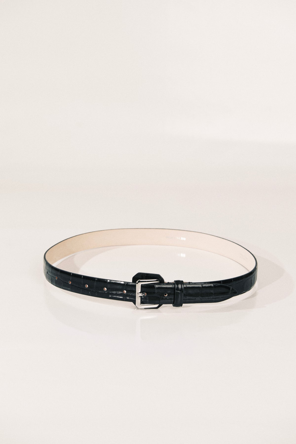 A black leather belt with a silver buckle, displayed in a circular shape on a clean white studio background.