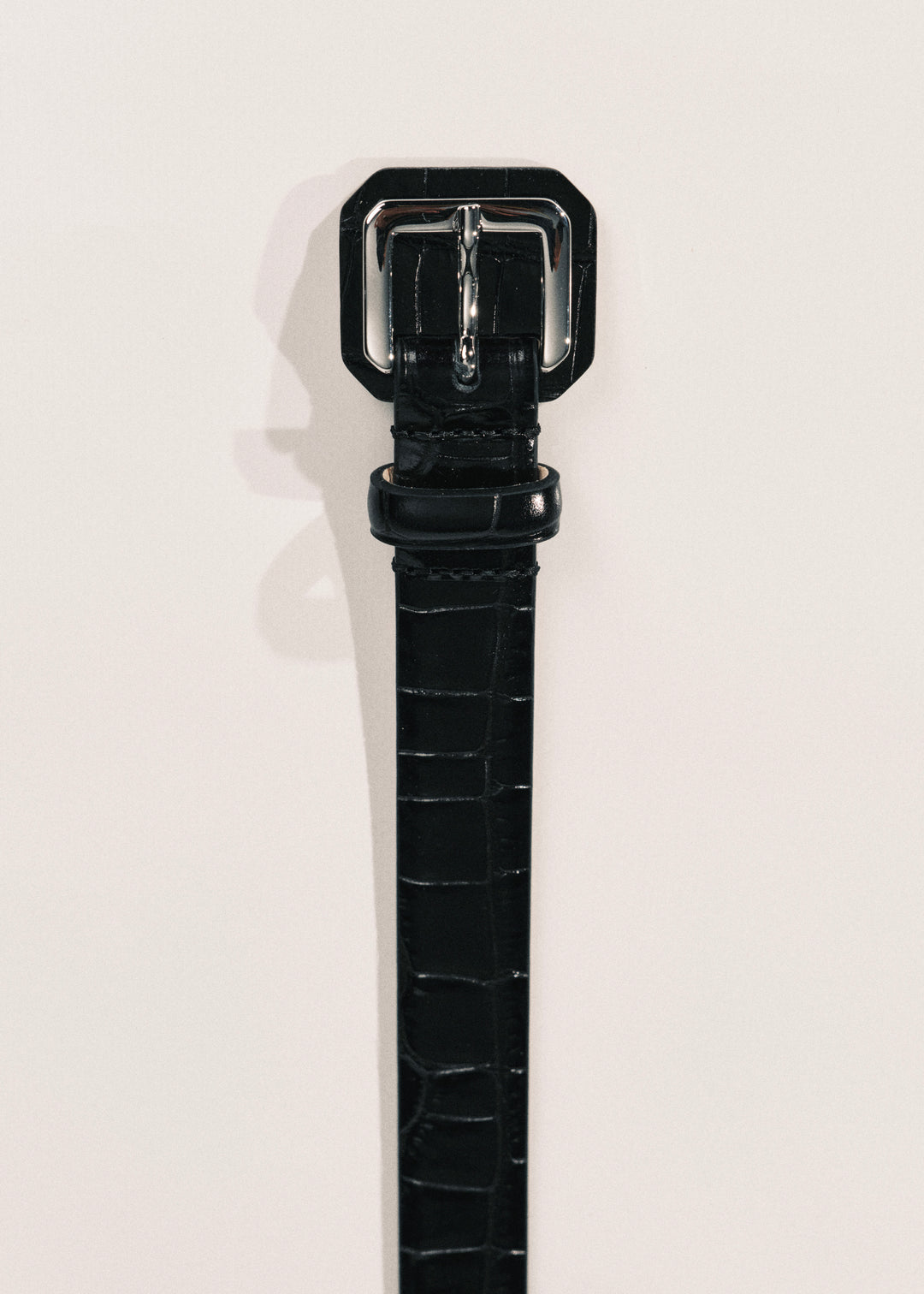 A close-up of a black alligator-embossed leather belt with a silver metal buckle. 