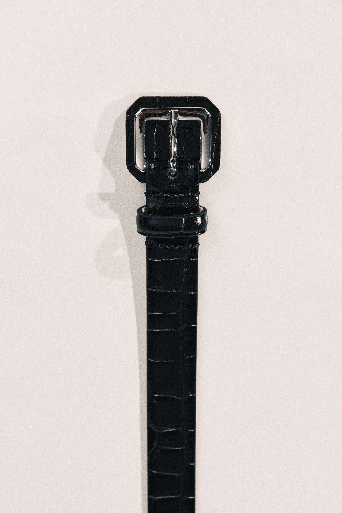 A close-up of a black alligator-embossed leather belt with a silver metal buckle. 