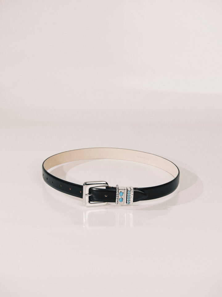 A slim black faux-leather belt with a silver-tone buckle and a decorative center clasp featuring light blue and white enamel details, displayed on a clean white studio background.