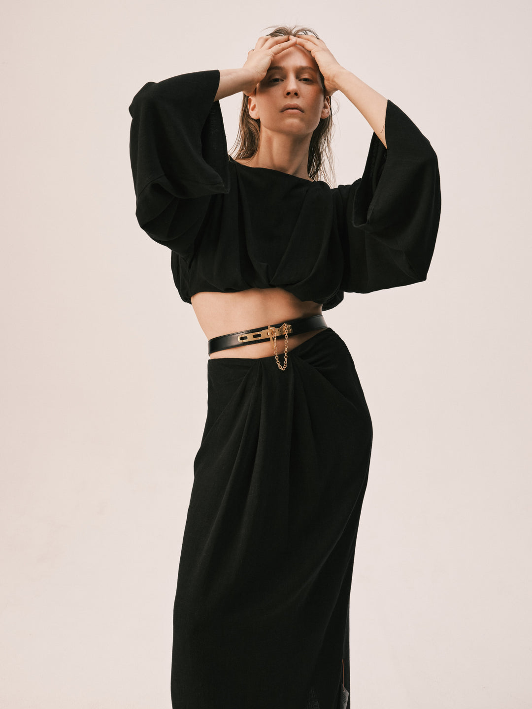  Elegant model in a black Déhanche Artemisia ensemble, featuring a stylish cropped top with dramatic sleeves and a high-waisted skirt with a chic belt.