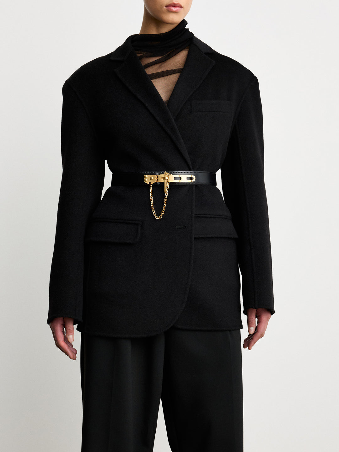 Déhanche Artemisia black leather belt with gold buckle and chain, paired with a chic black blazer, showcasing a sophisticated and elegant look.