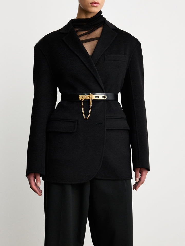 Déhanche Artemisia black leather belt with gold buckle and chain, paired with a chic black blazer, showcasing a sophisticated and elegant look.