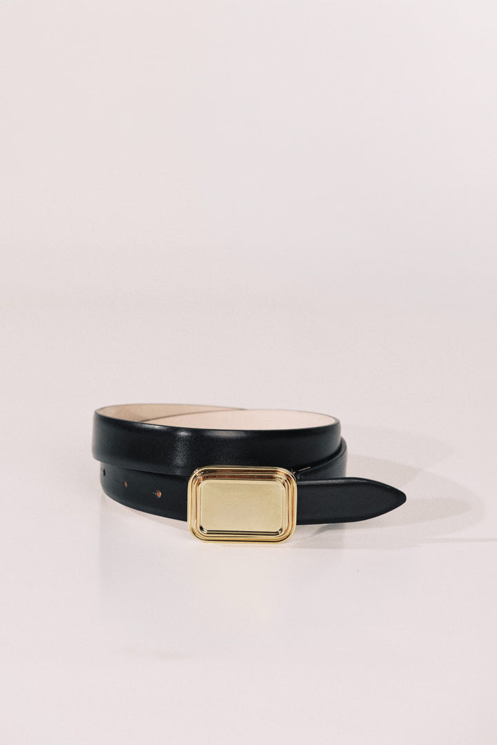 A black leather belt with a rectangular gold-tone metal buckle, neatly coiled on a light beige studio background.