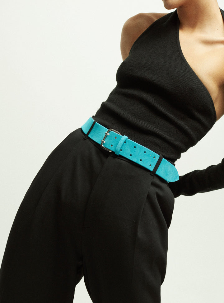 Close-up of a model wearing Déhanche hutch suede pants with a vibrant turquoise belt and a chic black sleeveless top, showcasing modern fashion.