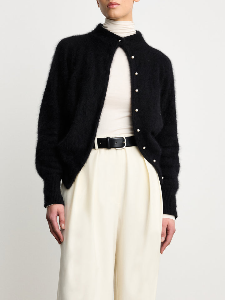 Model wearing Déhanche jeanne black leather belt with a silver buckle, paired with a black cardigan, white turtleneck, and cream pants, showcasing a refined look.