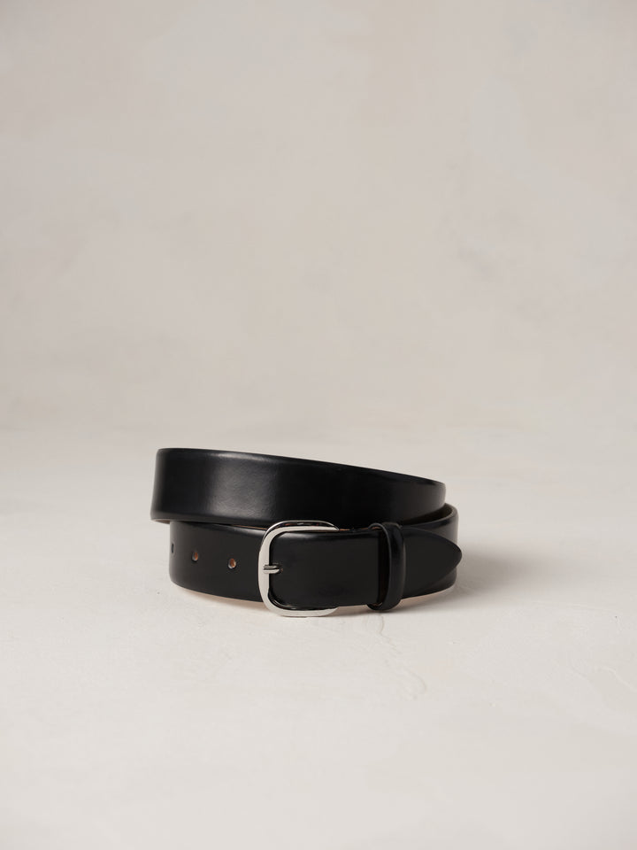 Déhanche jeanne belt in black leather with a silver buckle, elegantly coiled on a neutral background, showcasing high-quality craftsmanship and style.