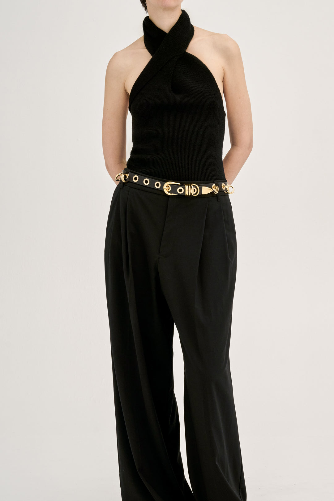 Model wearing Déhanche Revenge Gold black leather belt with gold grommets and buckle, styled with black trousers and a halter neck black top.