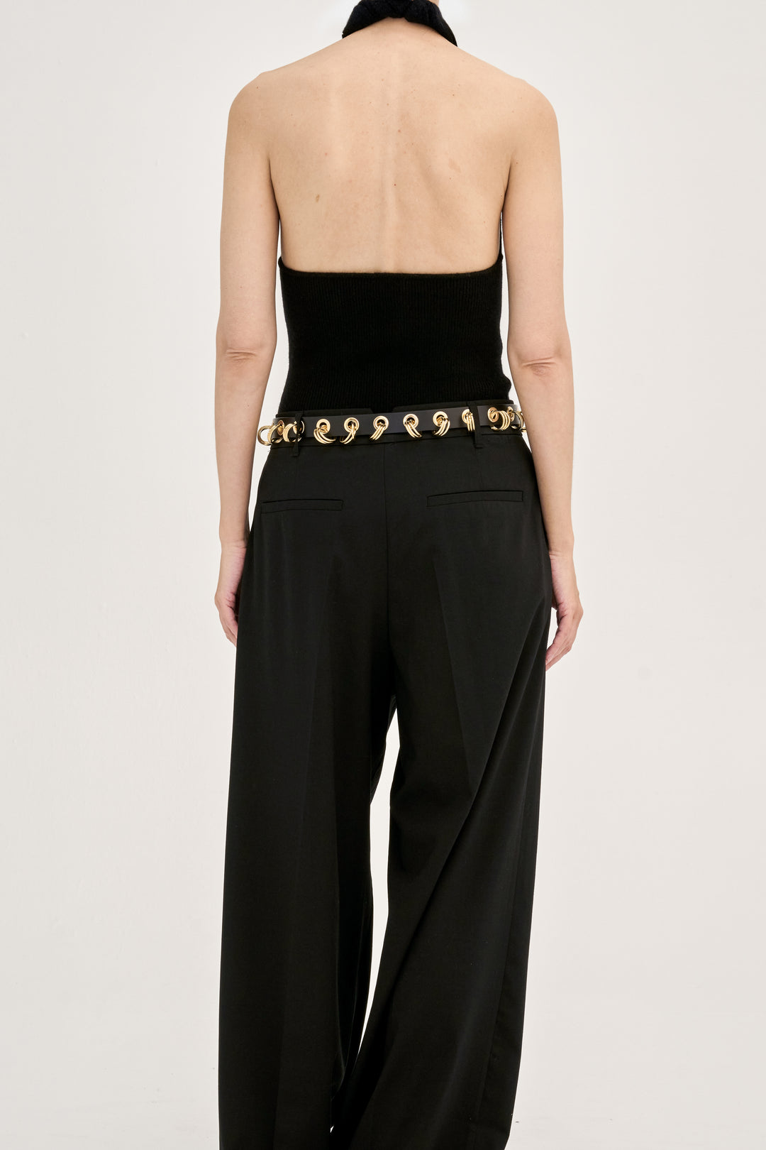 Model wearing Déhanche Revenge Gold black leather belt with gold grommets and buckle, styled with black trousers and a strapless black top, back view