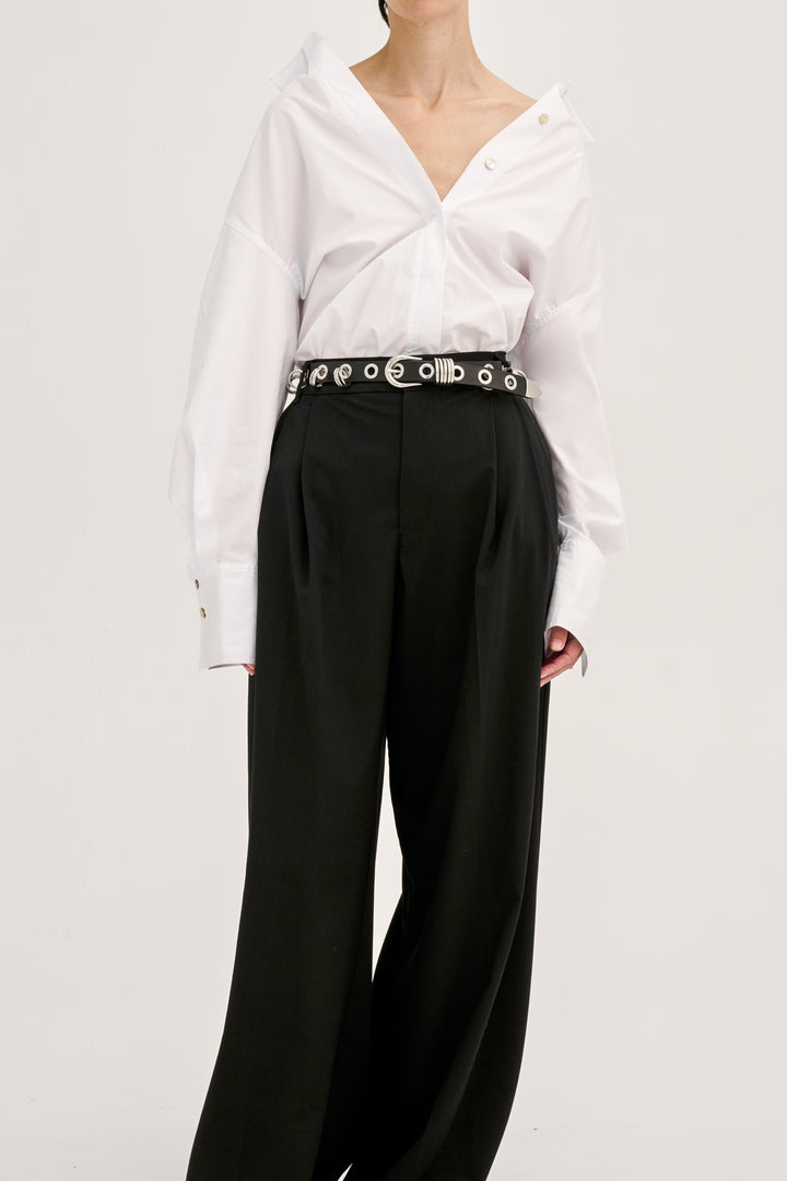 Déhanche Revenge Silver belt in black leather with silver grommets and buckle, worn with black high-waisted pants and a white blouse.