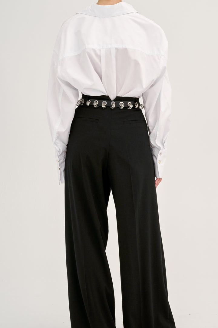 Déhanche Revenge Silver belt in black leather with silver grommets and buckle, worn with black high-waisted pants and a white blouse.
