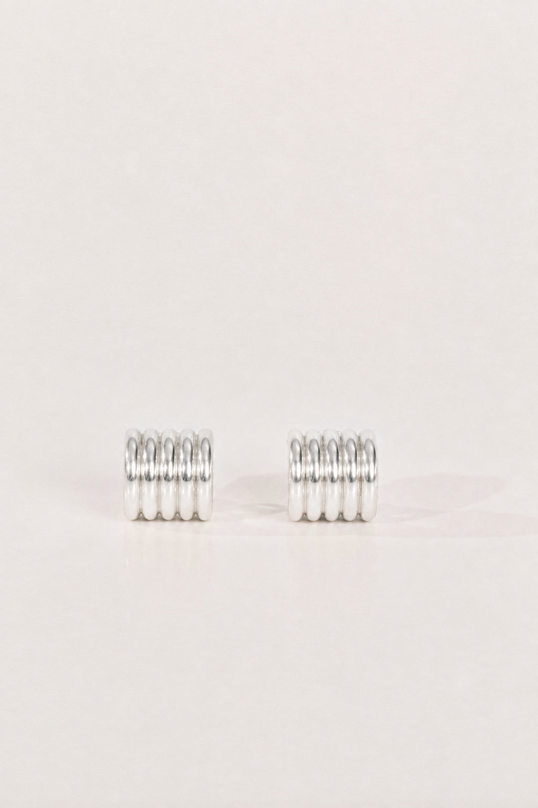 A pair of silver metal earrings, textured design, displayed on a clean, solid, light beige background.