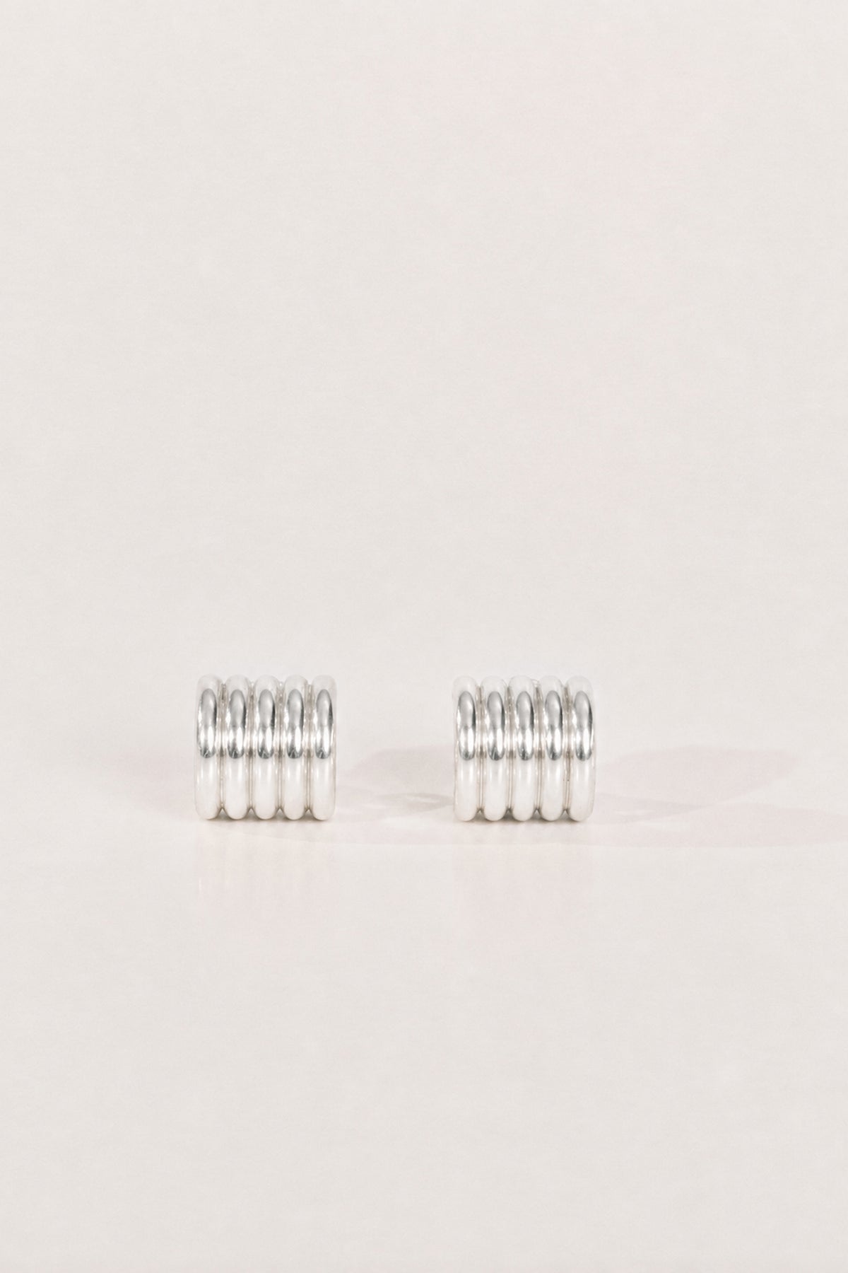 A pair of silver metal earrings, textured design, displayed on a clean, solid, light beige background.