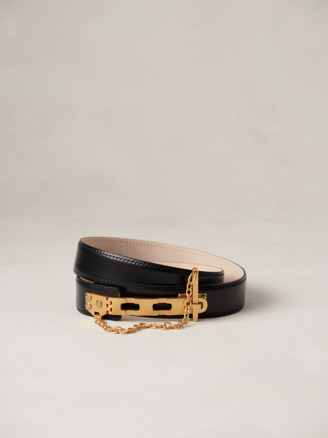 Déhanche Artemisia black leather belt with gold buckle and chain, featuring a minimalist design. Perfect accessory for elegant and chic outfits.