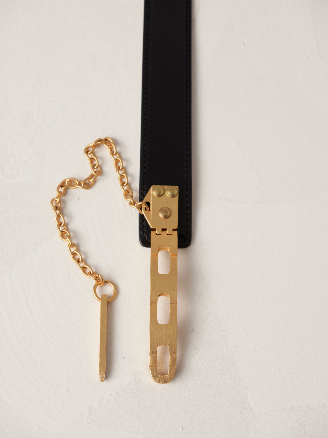 Close-up of Déhanche Artemisia belt, featuring a sleek black leather strap with a distinctive gold chain and hardware, showcasing elegance and sophistication.