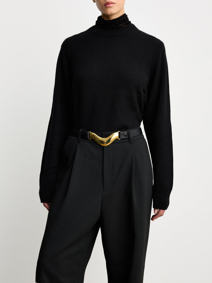 Model wearing a Déhanche Brancusi belt in sleek black leather with a sculptural gold centerpiece, styled over an all-black ensemble, embodying modern elegance.