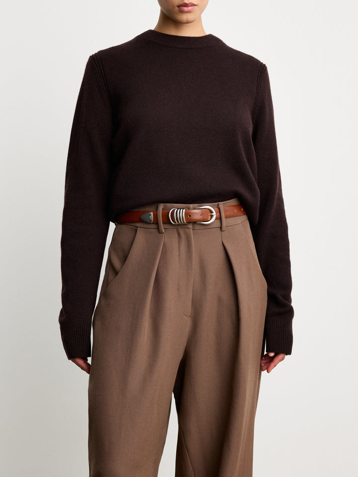 Model wearing Déhanche Hollyhock belt in rich brown leather with an intricate silver buckle, paired with a dark brown sweater and high-waisted trousers, showcasing a blend of classic and modern style.