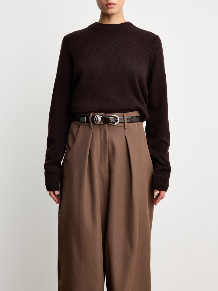 Déhanche Hollyhock Croco belt in dark brown crocodile leather paired with a cozy dark brown sweater and high-waisted trousers, epitomizing refined elegance.Déhanche Hollyhock Croco belt in dark brown crocodile leather paired with a cozy dark brown sweater and high-waisted trousers, epitomizing refined elegance.