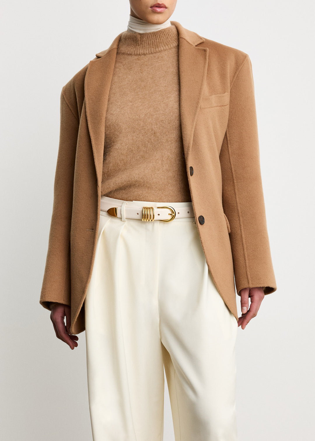 Déhanche Hollyhock Gold Belt - Elegant white leather belt with gold buckle, paired with a camel blazer, beige sweater, and white trousers. Sophisticated and chic outfit.
