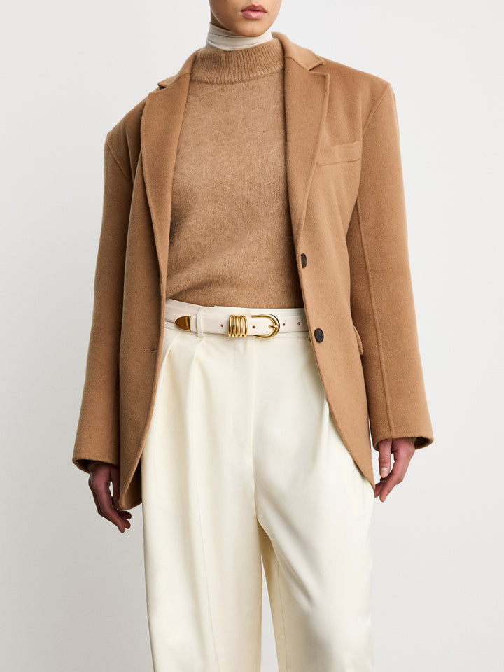 Déhanche Hollyhock Gold Belt - Elegant white leather belt with gold buckle, paired with a camel blazer, beige sweater, and white trousers. Sophisticated and chic outfit.