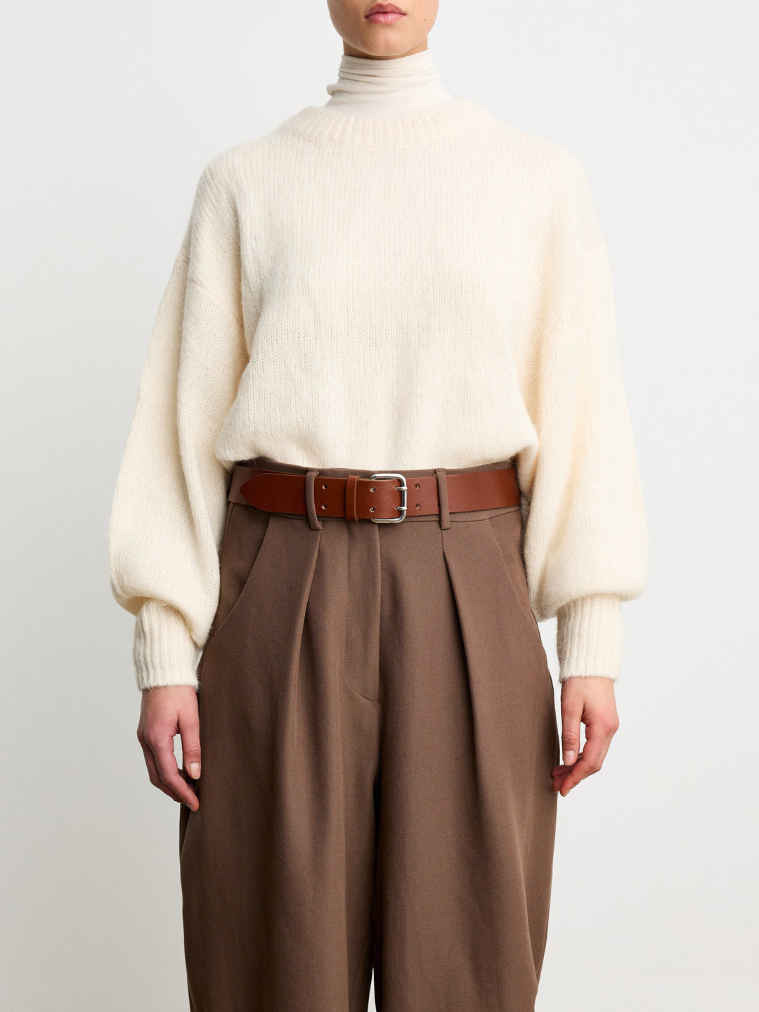 Déhanche Hutch Leather Belt - Classic brown leather belt with silver buckle, paired with brown trousers and a cream sweater. Ideal for a cozy, stylish look.