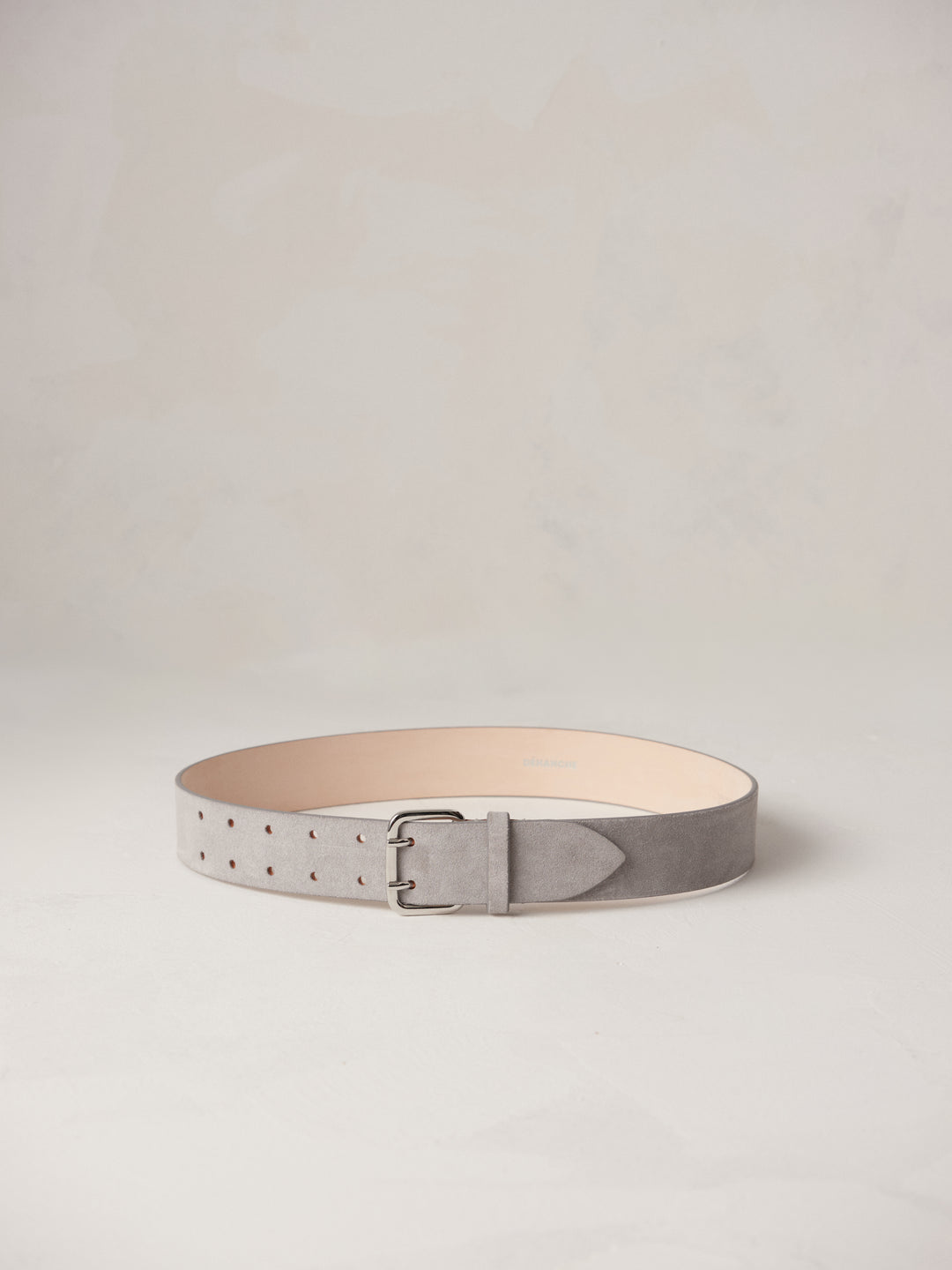 Déhanche hutch suede belt in light grey, elegantly coiled on a neutral background, featuring a sleek silver buckle and premium craftsmanship