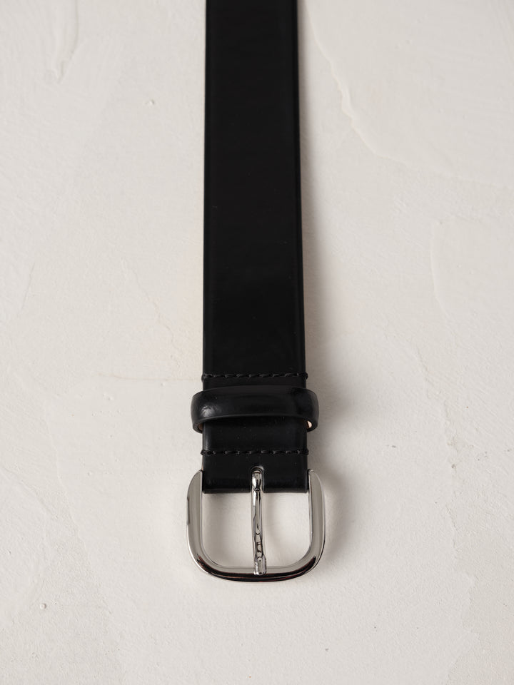 Déhanche jeanne belt in black leather with a silver buckle, elegantly coiled on a neutral background, showcasing high-quality craftsmanship and style.