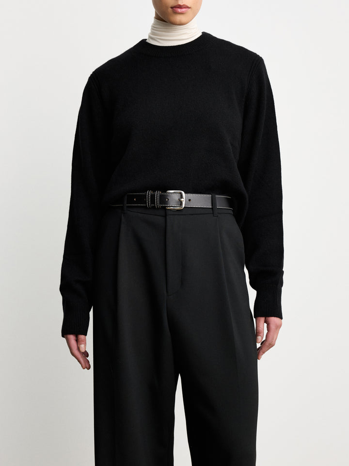 Model wearing Déhanche Louison black leather belt with white stitching and silver buckle, styled with black trousers and a black sweater