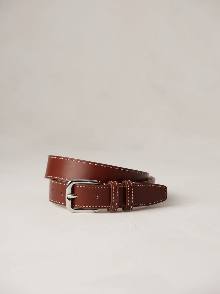 Déhanche louison belt in rich brown leather with white stitching and a silver buckle, elegantly coiled on a neutral background, showcasing refined craftsmanship.