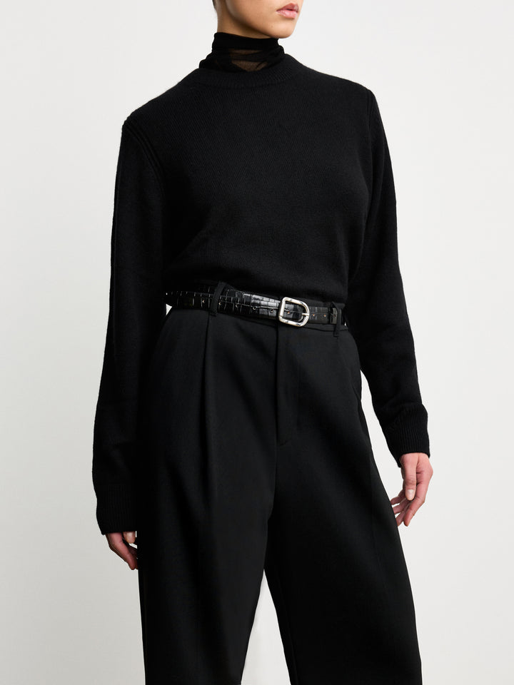 Model wearing Déhanche Mija Croco black leather belt with crocodile texture and silver buckle, styled with black trousers and a black turtleneck sweater.