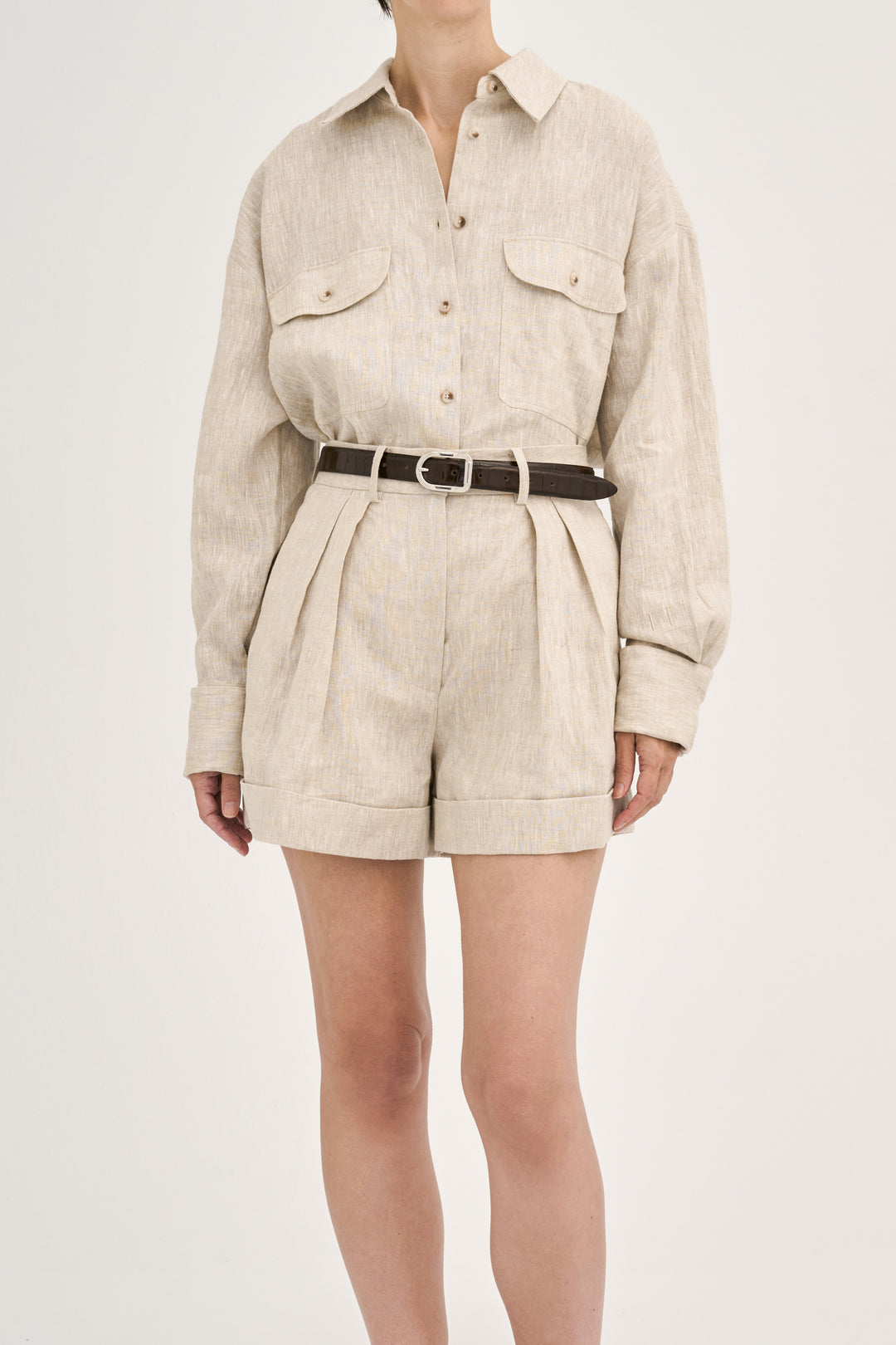 Model wearing Déhanche Mija Croco brown leather belt with crocodile texture and silver buckle, styled with beige linen shorts and matching shirt.