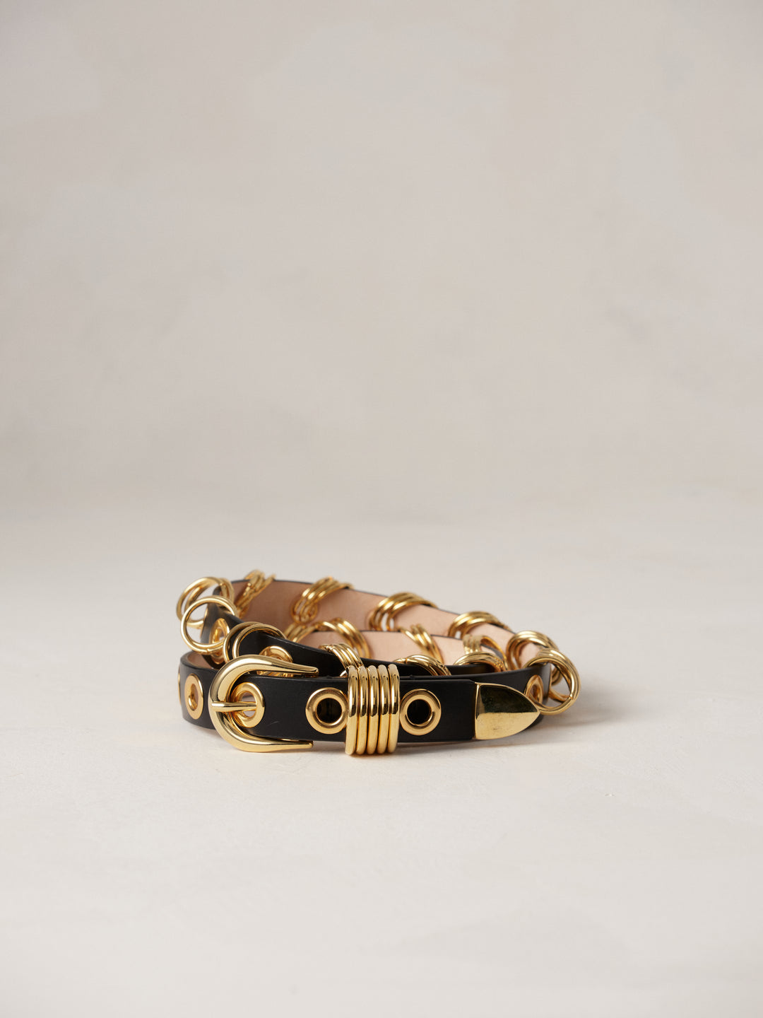 Déhanche Revenge Gold black leather belt with gold grommets and buckle, displayed against a light background.