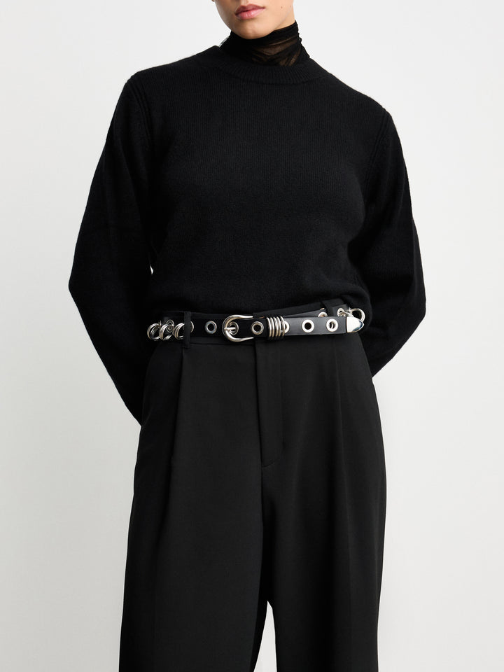 Déhanche Revenge Silver belt in black leather with silver grommets and buckle, worn with black high-waisted pants and a black sweater.