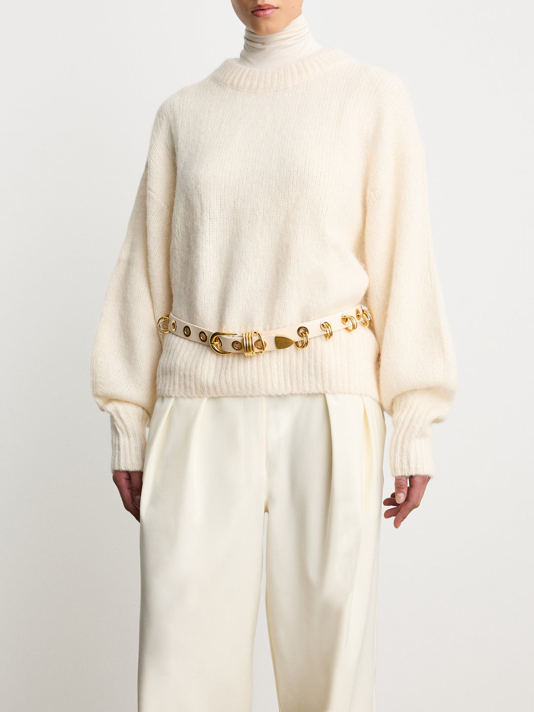Model wearing Déhanche Revenge Gold white leather belt with gold grommets and buckle, styled with cream trousers and a cream sweater.