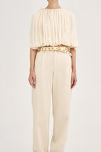 Model wearing Déhanche Revenge Gold white leather belt with gold grommets and buckle, styled with high-waisted cream pants and a flowy cream blouse.