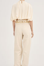 Model wearing Déhanche Revenge Gold white leather belt with gold grommets and buckle, styled with high-waisted cream pants and a flowy cream blouse, back view.