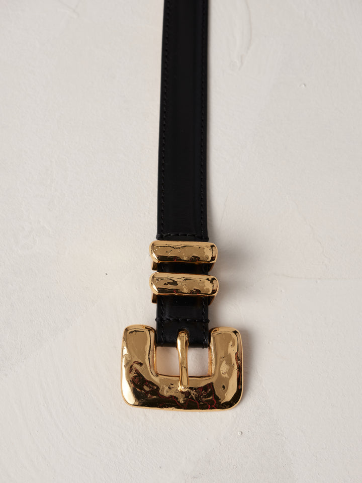 Déhanche tetre belt featuring black leather with a gold buckle and double loops, displayed on a neutral background.