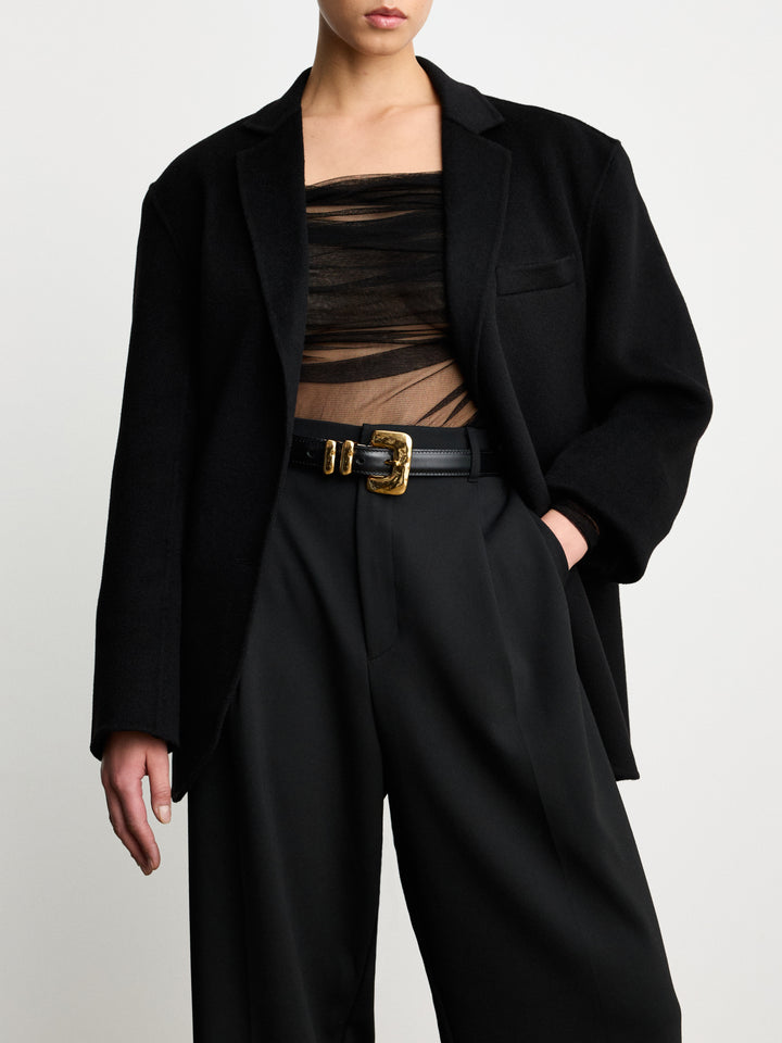 Déhanche Tetra belt in black leather with a unique gold buckle, styled with a sheer black top and black oversized blazer.