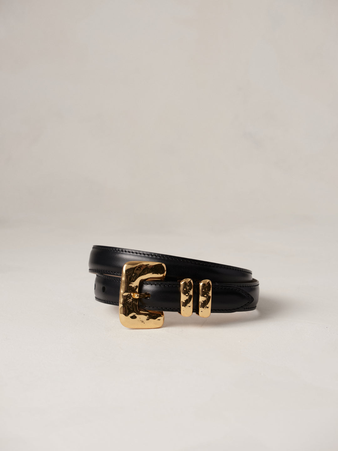 Déhanche tetre belt featuring black leather with a gold buckle and double loops, displayed on a neutral background.