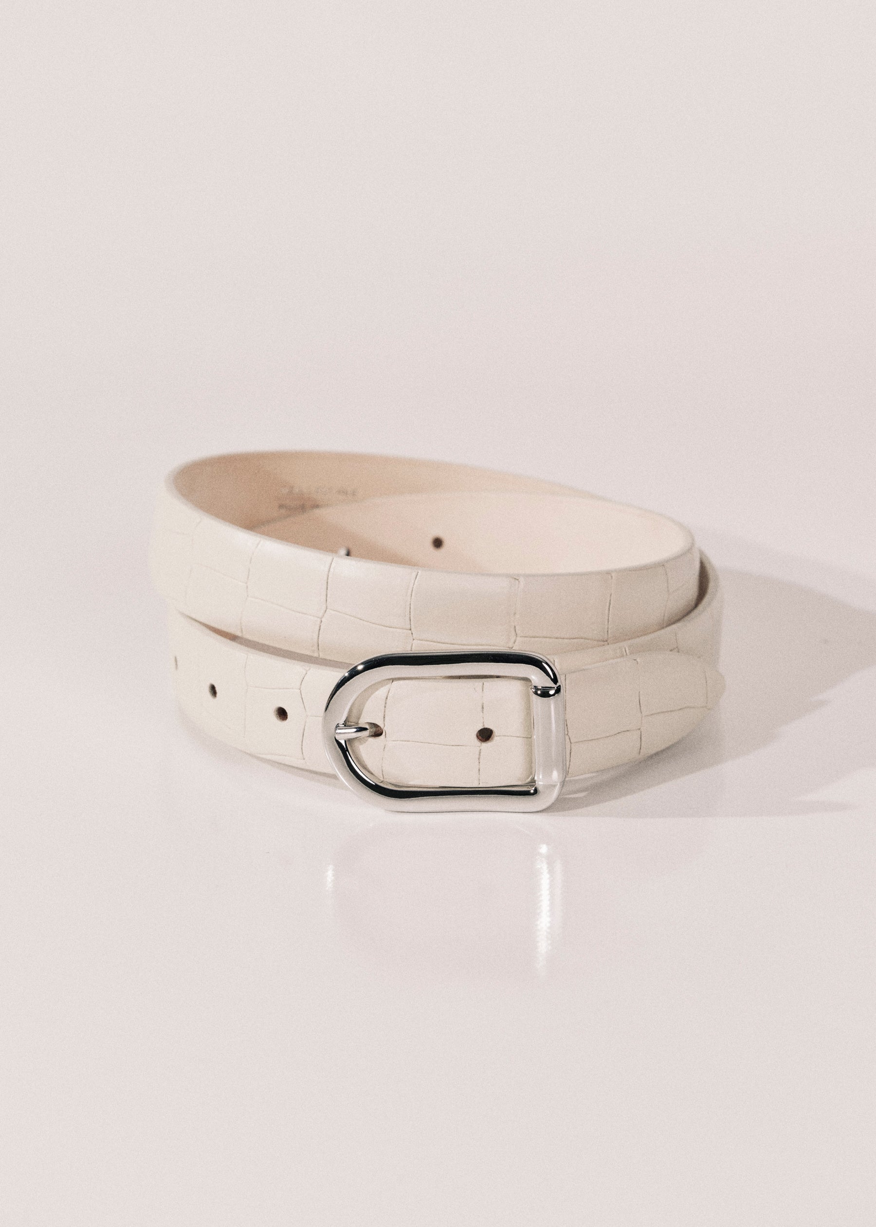 A ivory alligator-embossed leather belt with a polished silver-tone metal buckle. 