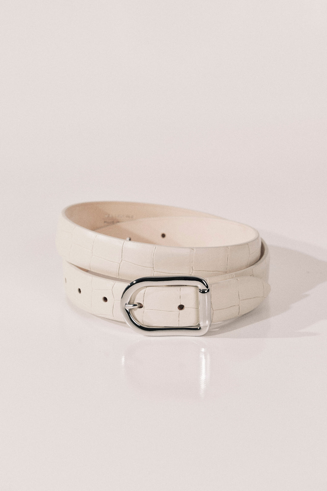 A ivory alligator-embossed leather belt with a polished silver-tone metal buckle. 