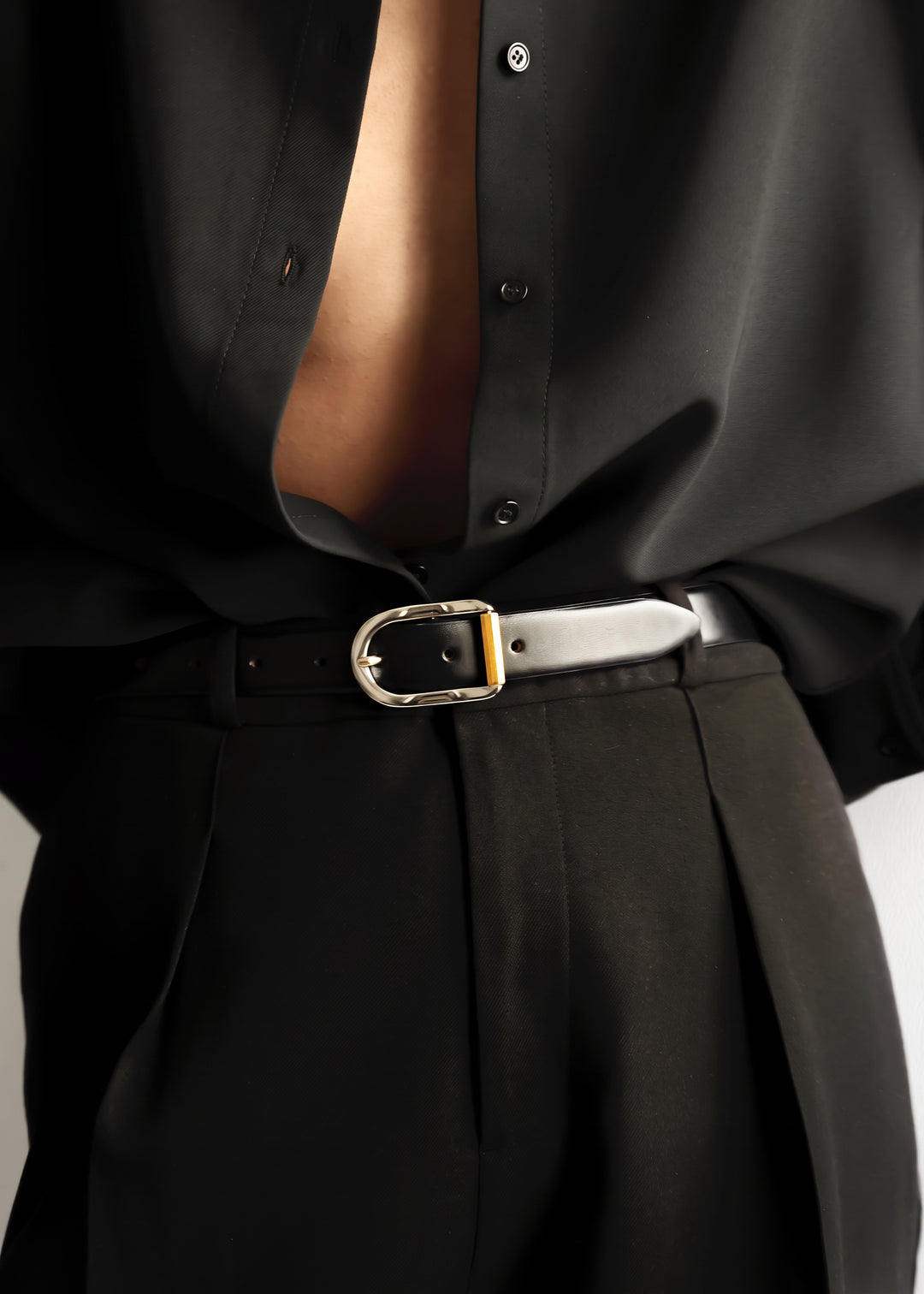 Model wearing a black shirt and black pants with a black belt with silver and gold hardware