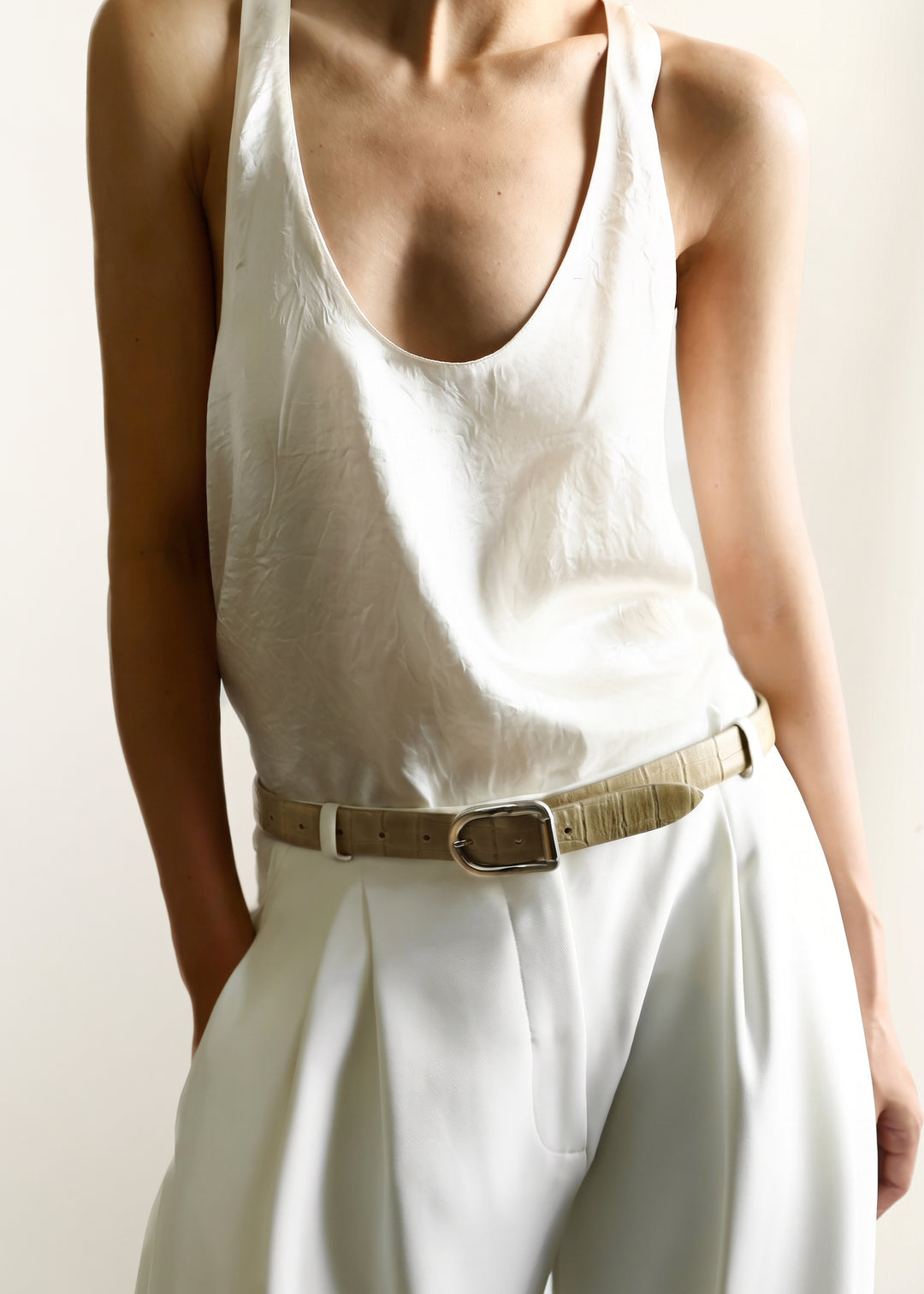 A model wearing a white sleeveless top and white trousers, cinched at the waist with a chai brown alligator textured belt with silver hardware
