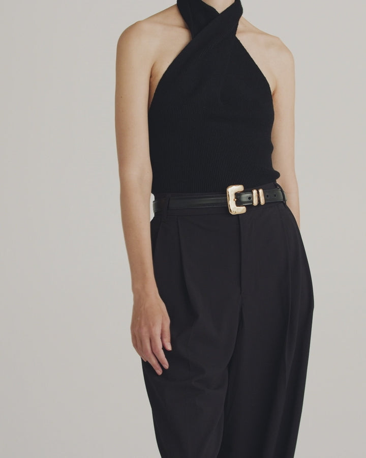 Déhanche Tetra belt in black leather with a distinctive gold buckle, worn with a black halter top and high-waisted black pants.