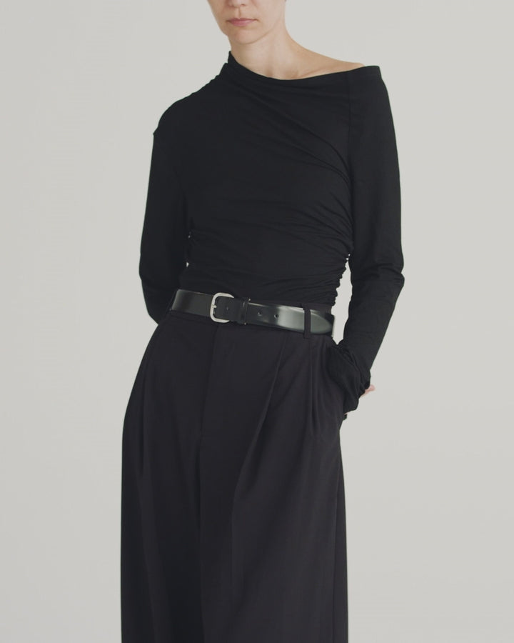 Model wearing Déhanche jeanne black leather belt with a silver buckle, paired with a black asymmetrical top and black pants, highlighting an elegant and modern style.