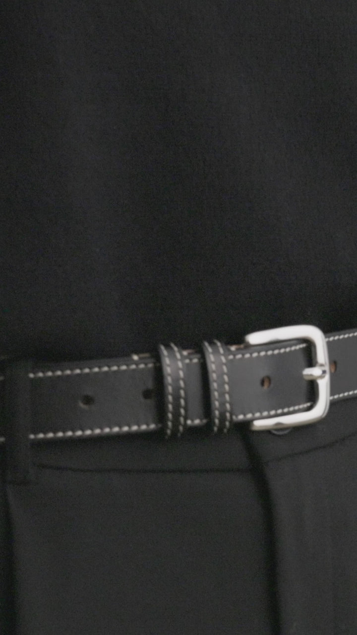 Model wearing Déhanche Louison black leather belt with white stitching and silver buckle, styled with black trousers and a black sweater