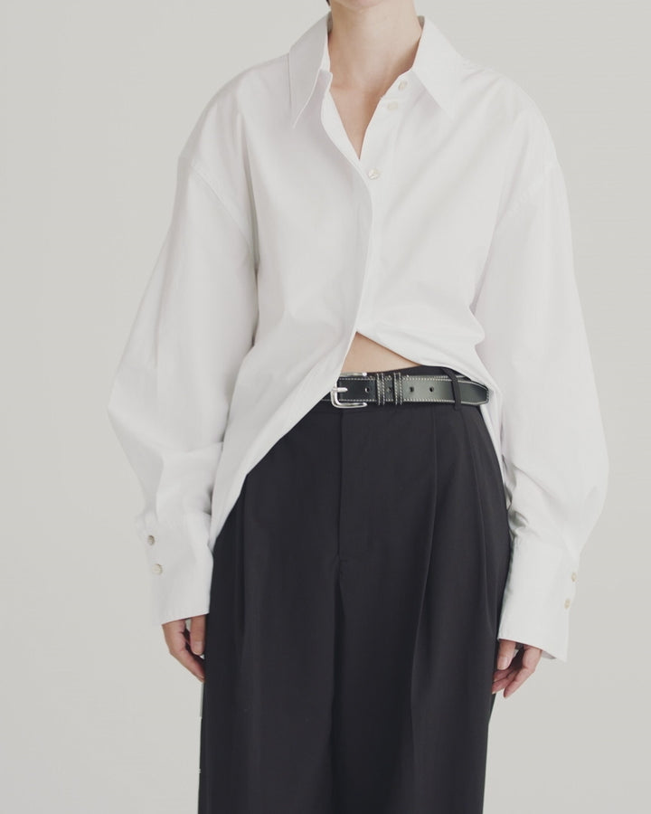 Model showcasing Déhanche Louison black leather belt with white stitching and silver buckle, paired with black trousers and an oversized white shirt.