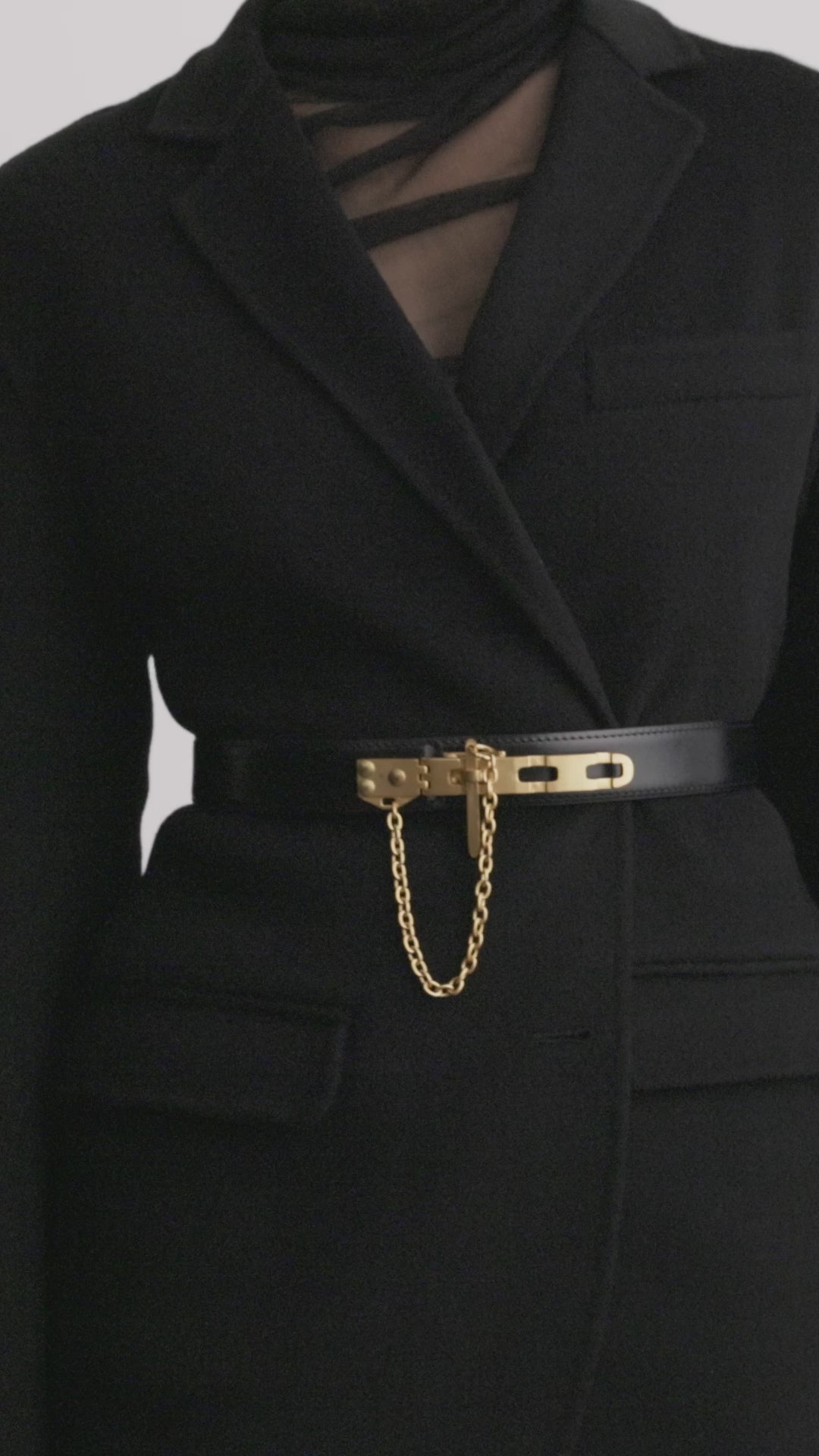Déhanche Artemisia black leather belt with gold buckle and chain, showcased on a model wearing a chic black blazer, highlighting its elegant design.